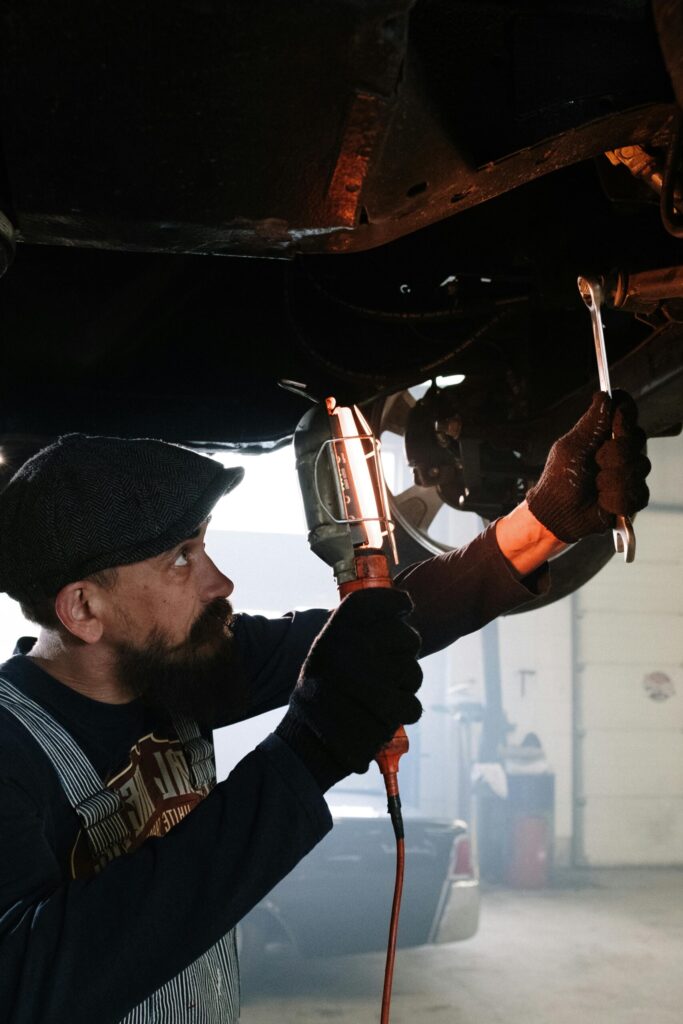 pexels photo 4489713 4489713 A bearded auto mechanic working diligently under a car in a garage.